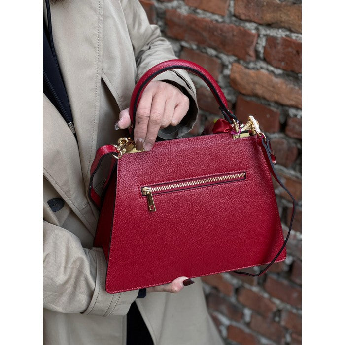 A red leather handbag with gold-tone metal details and a decorative scarf attached to the handle.
