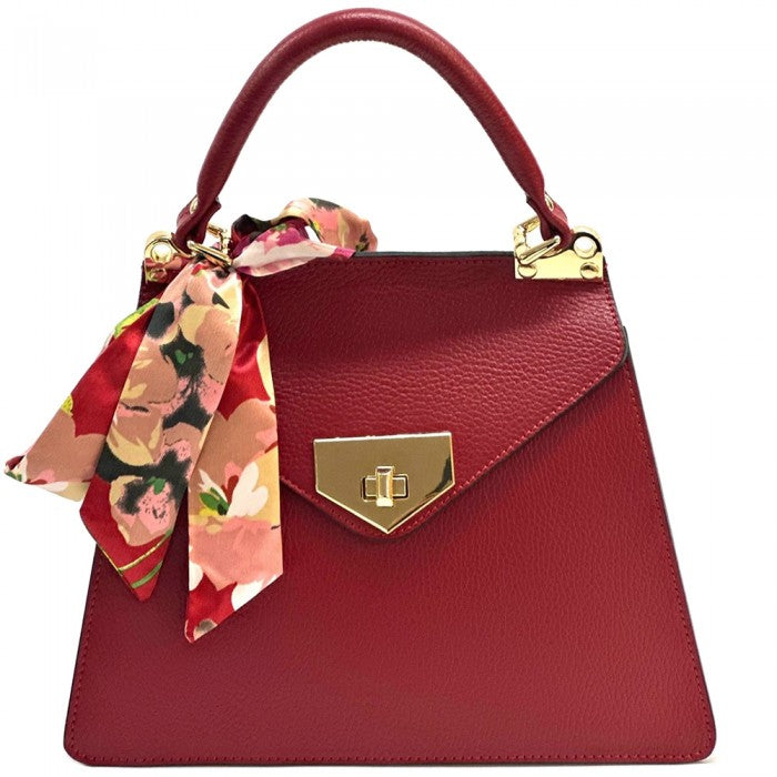 A red leather handbag with gold-tone metal details and a decorative scarf tied to the handle.