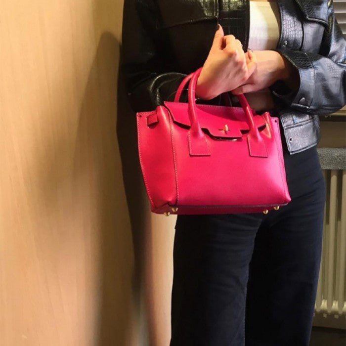 A pink Italian leather handbag with a structured design, double handles, and a gold-tone clasp.