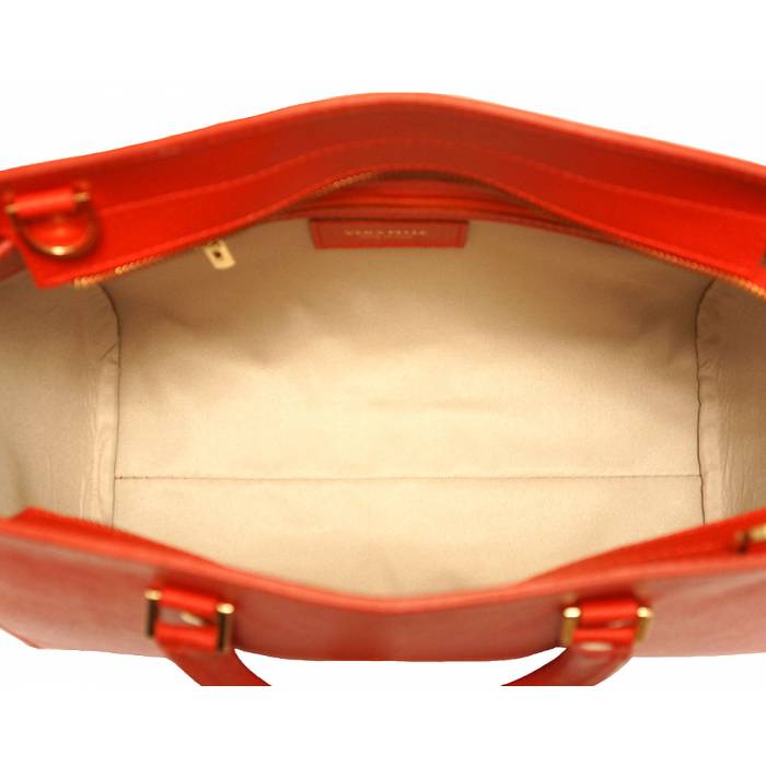 A red leather handbag with golden metal hardware and a decorative tag on one of the handles.