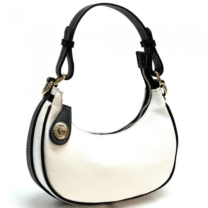 A white Noemi leather handbag with a pebble-grain texture, featuring a crescent shape, vintage brass hardware, a detachable shoulder strap, and a top handle.