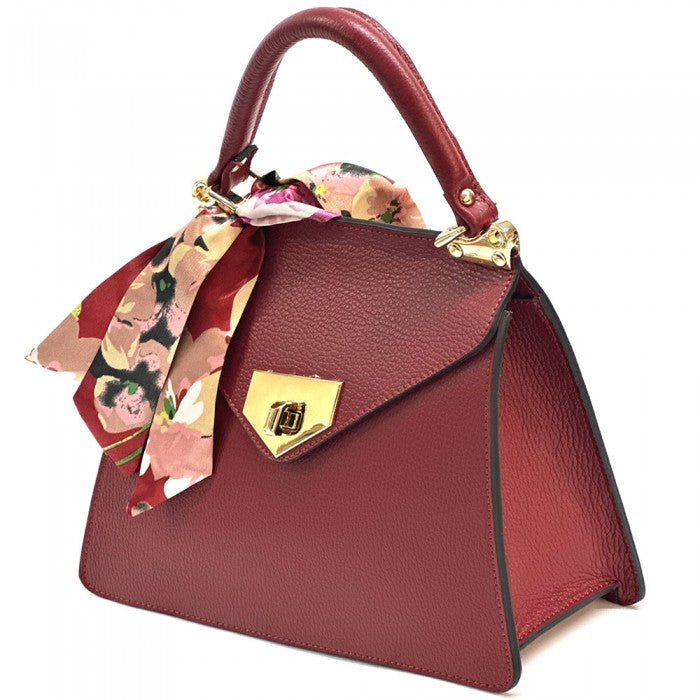 A  red leather handbag with gold-tone metal details and a decorative scarf attached to the handle.