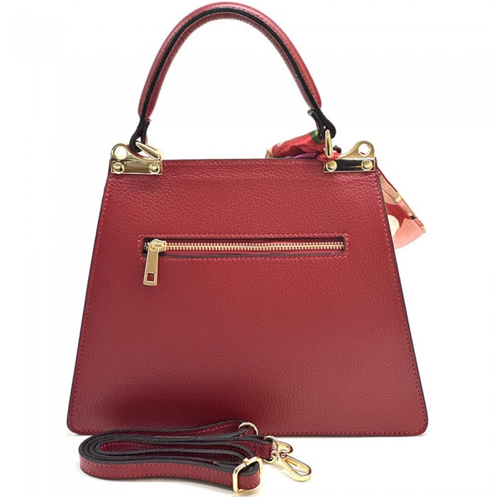 A  red leather handbag with gold-tone metal details and a decorative scarf attached to the handle.