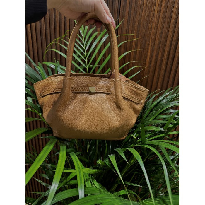 A brown Terra Italian handmade leather handbag displayed against a wooden background with green foliage in the foreground.